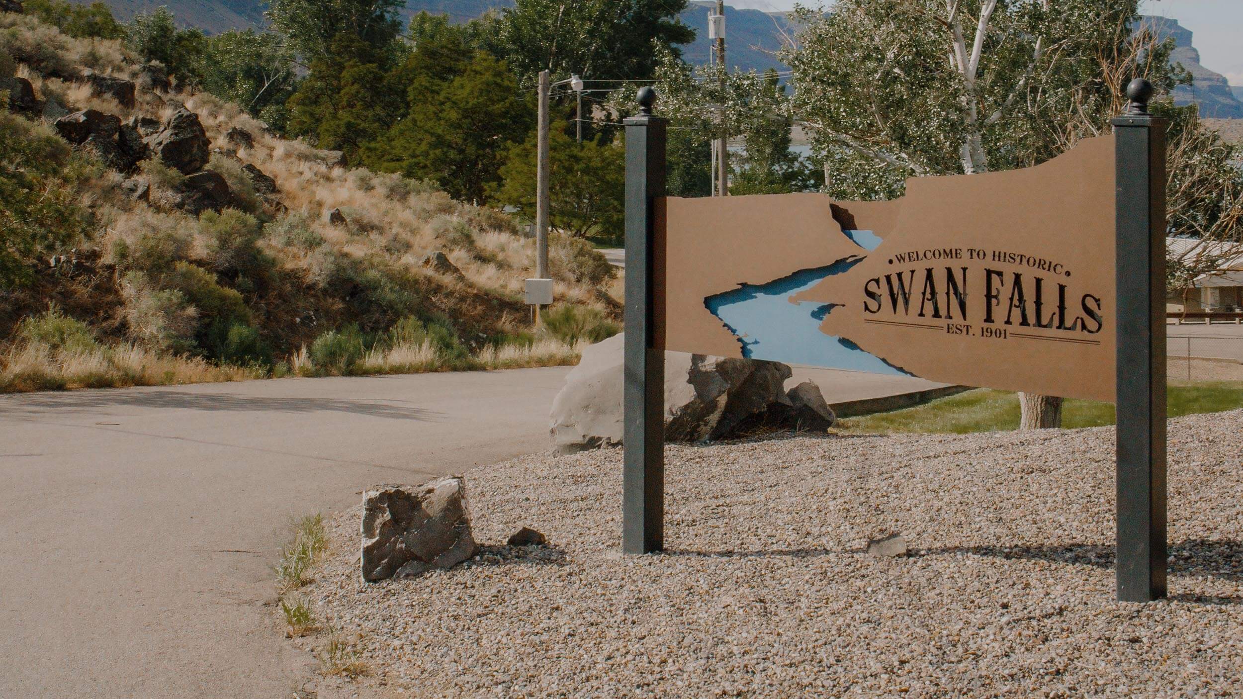 a sign for swan falls on the side of a road with trees in the background